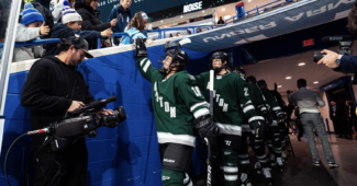 Members of PWHL Boston, wearing green jerseys, exit the locker room tunnel and high-fans prior to a game against PWHL Minnesota.